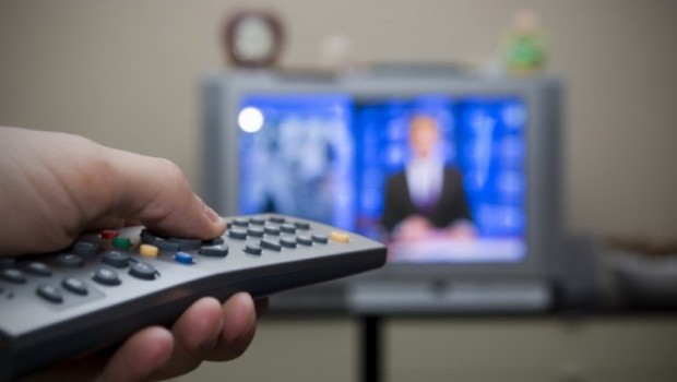 mão segurando controle remoto e propaganda eleitoral passando na televisão
