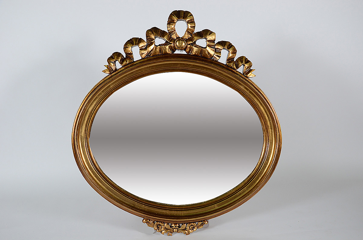 Espelho de cristal feitio oval com moldura dourada encimada por...