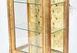 Vitrine de madeira dourada estilo francês, 2 pr... - Vitrine de madeira dourada estilo francês, 2 prateleiras de vidro, fundo com tecido capitone, tampo de mármore.