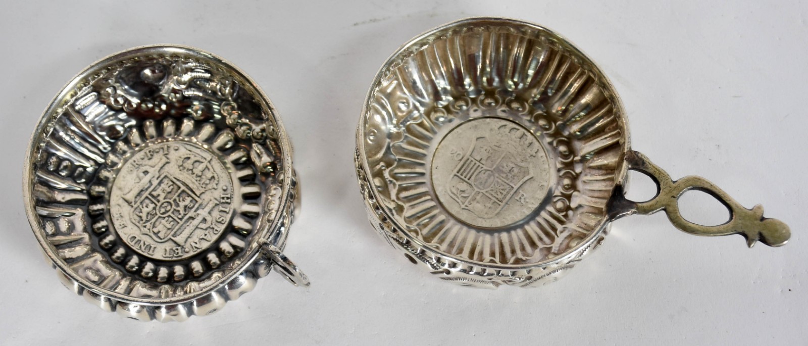 Dois provadores de vinho de prata de lei com moedas ao fundo. (por... - foto 2 de 4