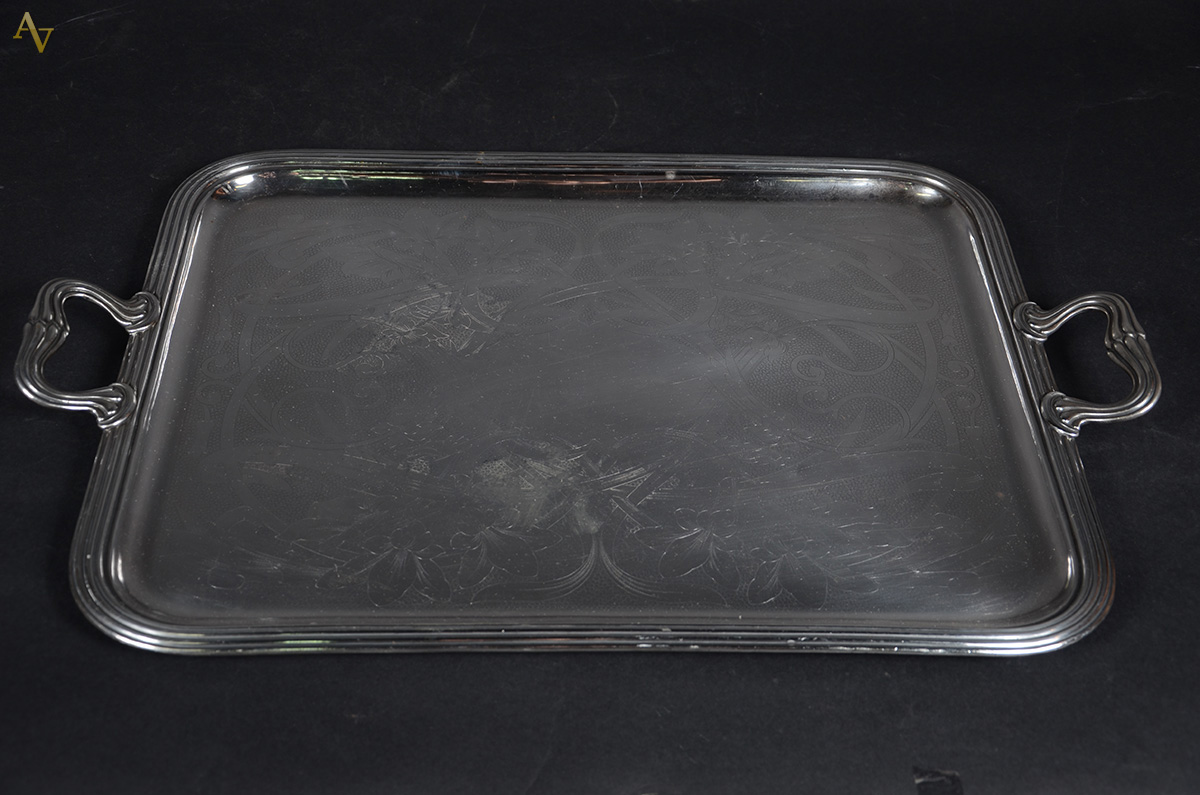 Bandeja de metal prateado com alças, fundo ricamente cinzelado com...