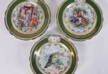 Três pratos de porcelana europeia monogramada, ... - Três pratos de porcelana europeia monogramada, dois deles decorados com figuras femininas e o terceiro com figura de peixe em policromia, bordas...