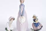 Lladró (1953),  - Três estatuetas de porcelana espanhola policromada representando moça com chapéu, menina com vaso de flores e menina com chapéu ao vento.