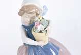 Lladró (1953),  - Três estatuetas de porcelana espanhola policromada representando moça com chapéu, menina com vaso de flores e menina com chapéu ao vento.