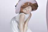 Lladró (1953),  - Três estatuetas de porcelana espanhola policromada representando moça com chapéu, menina com vaso de flores e menina com chapéu ao vento.