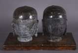 Duas cabeças orientais de pedra, apoiadas em ba... - Duas cabeças orientais de pedra, apoiadas em base de madeira, parte dos selos ainda no topo da cabeça.