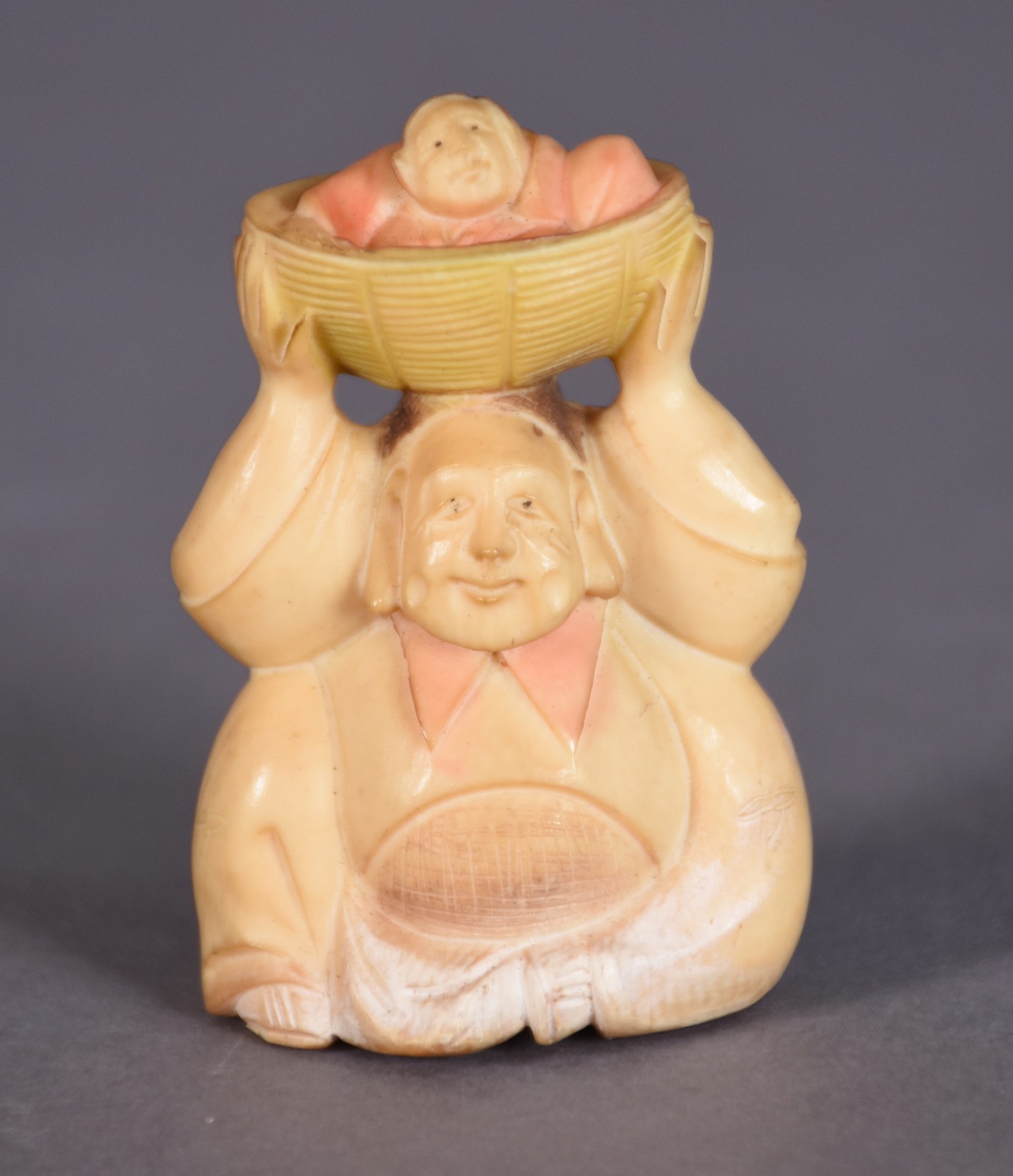 Netsuke de marfim representando figura segurando criança no cesto... - foto 1 de 3
