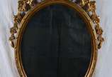 Espelho oval com moldura dourada encimado por f... - Espelho oval com moldura dourada encimado por florão entalhado. Med: 100 x 60 cm