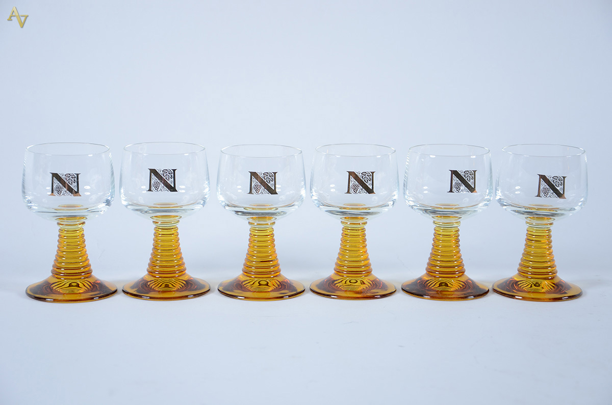 Seis cálices para vinho com base amarela e letra N em dourado.
