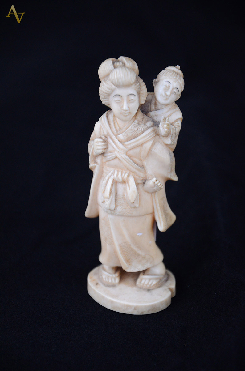 Estatueta de marfim repres. mulher com criança nas costas. Assinado...