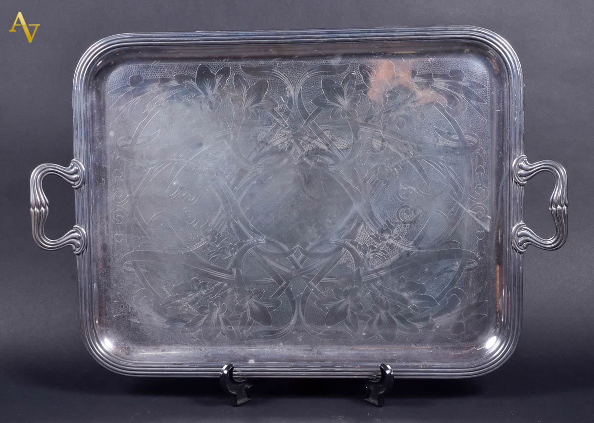Bandeja de metal prateado com alças, fundo cinzelado com guirlandas...