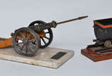 Duas miniaturas, sendo uma de canhão com base d... - Duas miniaturas, sendo uma de canhão com base de mármore, med. 36 x 16 cm e outra de vagão de trem, base med. 11 x 18 cm.