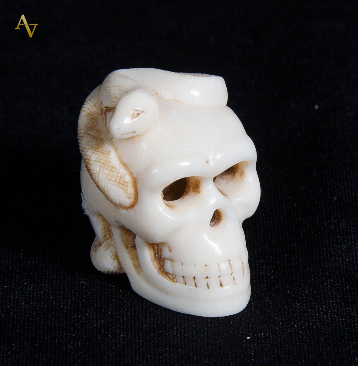 Netsuke de marfim, representando caveira com cobra. Alt. 3cm.