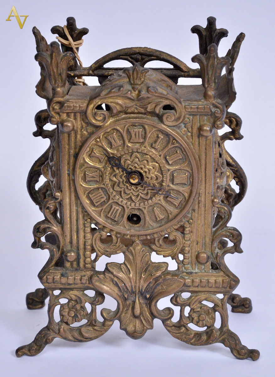 Relógio de bronze com algarismos romanos e folhagens vazadas. alt...