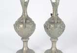 Par de ânforas de metal com anjos, flores e fol... - Par de ânforas de metal com anjos, flores e folhagens em relevo. Uma delas com aplique de figura alada estilizada. Desgastes no metal.
