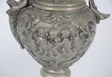 Par de ânforas de metal com anjos, flores e fol... - Par de ânforas de metal com anjos, flores e folhagens em relevo. Uma delas com aplique de figura alada estilizada. Desgastes no metal.
