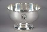 Grande bowl de metal prateado, bordas com cordo... - Grande bowl de metal prateado, bordas com cordoados, pegas laterais na forma de cabeças de leão em relevo com argolas. Desgastes.