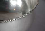 Grande bowl de metal prateado, bordas com cordo... - Grande bowl de metal prateado, bordas com cordoados, pegas laterais na forma de cabeças de leão em relevo com argolas. Desgastes.