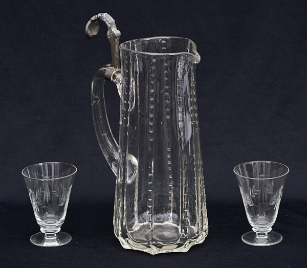 Dez copinhos de cristal para licor e uma jarra com detalhe de metal.
