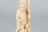 Escultura de marfim representando Shou Xing, o ... - Escultura de marfim representando Shou Xing, o deus da Longevidade, com figura de criança aos seus pés. Segura o pêssego e traz o cajado feito t...