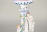 Fruteira de porcelana alemã policromada, base c... - Fruteira de porcelana alemã policromada, base com figura feminina recostada em coluna olhando para figura angelical com guirlandas florais, prat...