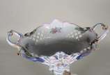 Fruteira de porcelana alemã policromada, base c... - Fruteira de porcelana alemã policromada, base com figura feminina recostada em coluna olhando para figura angelical com guirlandas florais, prat...