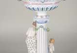 Fruteira de porcelana alemã policromada, base c... - Fruteira de porcelana alemã policromada, base com figura feminina recostada em coluna olhando para figura angelical com guirlandas florais, prat...