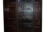 Grande vitrine de madeira nobre com duas portas... - Grande vitrine de madeira nobre com duas portas de correr de vidro e 4 prateleiras internas. Pequena parte quebrada e colada na porta de vidro.