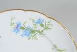 Limoges (1771),  - Prato de sobremesa de porcelana francesa Limoges, monogramado, decorado com flores em tons de azul e verde, borda recortada e realçada em dourado.