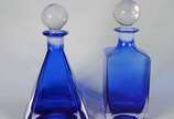 Duas garrafas de cristal na cor azul, sendo uma... - Duas garrafas de cristal na cor azul, sendo uma na forma de pirâmide e outra quadrangular, tampas em "bola".