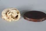 Netsuke de marfim representando figura típica c... - Netsuke de marfim representando figura típica com criança, base de madeira.