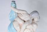 Relógio de mesa encimado por grupo escultórico ... - Relógio de mesa encimado por grupo escultórico de porcelana representando casal se beijando. Com pequenos desgastes e pequenos quebrados, pescoç...