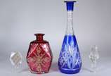 Duas garrafas, sendo uma facetada na cor rubi c... - Duas garrafas, sendo uma facetada na cor rubi com guirlandas douradas e outra de cristal doublé azul lapidada (esta última com gargalo trincado ...