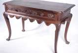 Mesa de madeira nobre com gavetão entalhado, sa... - Mesa de madeira nobre com gavetão entalhado, saia recortada e pernas ligeiramente recurvas (folheado do tampo descascando).