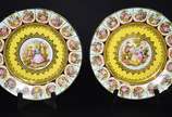 Par de medalhões de porcelana "Dom Pedro" decor... - Par de medalhões de porcelana "Dom Pedro" decorados com cenas românticas em policromia sobre fundo amarelo e guirlandas douradas.