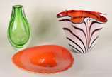 Três peças decorativas de vidro, sendo: vaso ve... - Três peças decorativas de vidro, sendo: vaso verde; centro de mesa laranja com bolhas internas; vaso feitio "lenço" com listras sobre fundo branco.