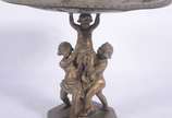 Centro de mesa/fruteira de bronze, base decorad... - Centro de mesa/fruteira de bronze, base decorada com figuras de "Pucci" sustentando o prato trabalhado com rostos e folhagens rem relevo.