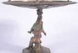 Centro de mesa/fruteira de bronze, base decorad... - Centro de mesa/fruteira de bronze, base decorada com figuras de "Pucci" sustentando o prato trabalhado com rostos e folhagens rem relevo.