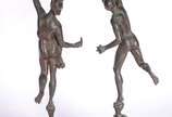 Par de castiçais de metal com figuras de casal ... - Par de castiçais de metal com figuras de casal de atletas segurando "tochas", apoiados em uma das pernas que estão sobre "cabeças" deitadas na b...