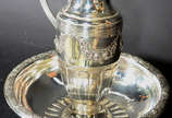 Jarra com bacia de metal prateado com guirlanda... - Jarra com bacia de metal prateado com guirlandas florais em relevo.