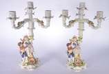 Par de candelabros de porcelana alemã para 4 ve... - Par de candelabros de porcelana alemã para 4 velas cada, decorados com figuras infantis camponeses e flores em relevo policromado. Marcados na b...