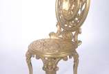 Cadeira de metal dourado trabalhado em relevo, ... - Cadeira de metal dourado trabalhado em relevo, encosto com medalhão decorado com figura de lenhador, assento com detalhes vazados.