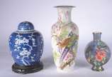 Três peças de porcelana ao gosto oriental, send... - Três peças de porcelana ao gosto oriental, sendo potiche com base de madeira (tampa quebrada) e 2 vasos, sendo um com fundo branco e flores em p...