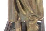 Estatueta de metal patinado representando figur... - Estatueta de metal patinado representando figura feminina com pássaro, acompanha coluna com tampo de vidro (metal com oxidação e desgastes).