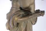 Estatueta de metal patinado representando figur... - Estatueta de metal patinado representando figura feminina com pássaro, acompanha coluna com tampo de vidro (metal com oxidação e desgastes).