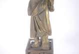 Estatueta de metal patinado representando figur... - Estatueta de metal patinado representando figura feminina com pássaro, acompanha coluna com tampo de vidro (metal com oxidação e desgastes).