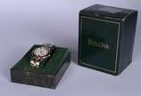Bulova (1875),  - Relógio de pulso com caixa, pulseira, números e ponteiros em aço com dourado. No estojo, funcionando.