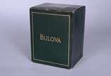 Bulova (1875),  - Relógio de pulso com caixa, pulseira, números e ponteiros em aço com dourado. No estojo, funcionando.