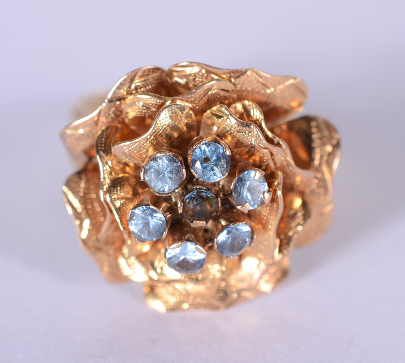 Anel de ouro 18 k., com flor cravejada de pedras azuis, aro 17. (Por... - foto 1 de 6