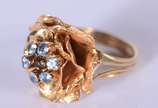 Anel de ouro 18 k., com flor cravejada de pedra... - Anel de ouro 18 k., com flor cravejada de pedras azuis, aro 17. (Por motivos de segurança a peça não se encontra na loja).
